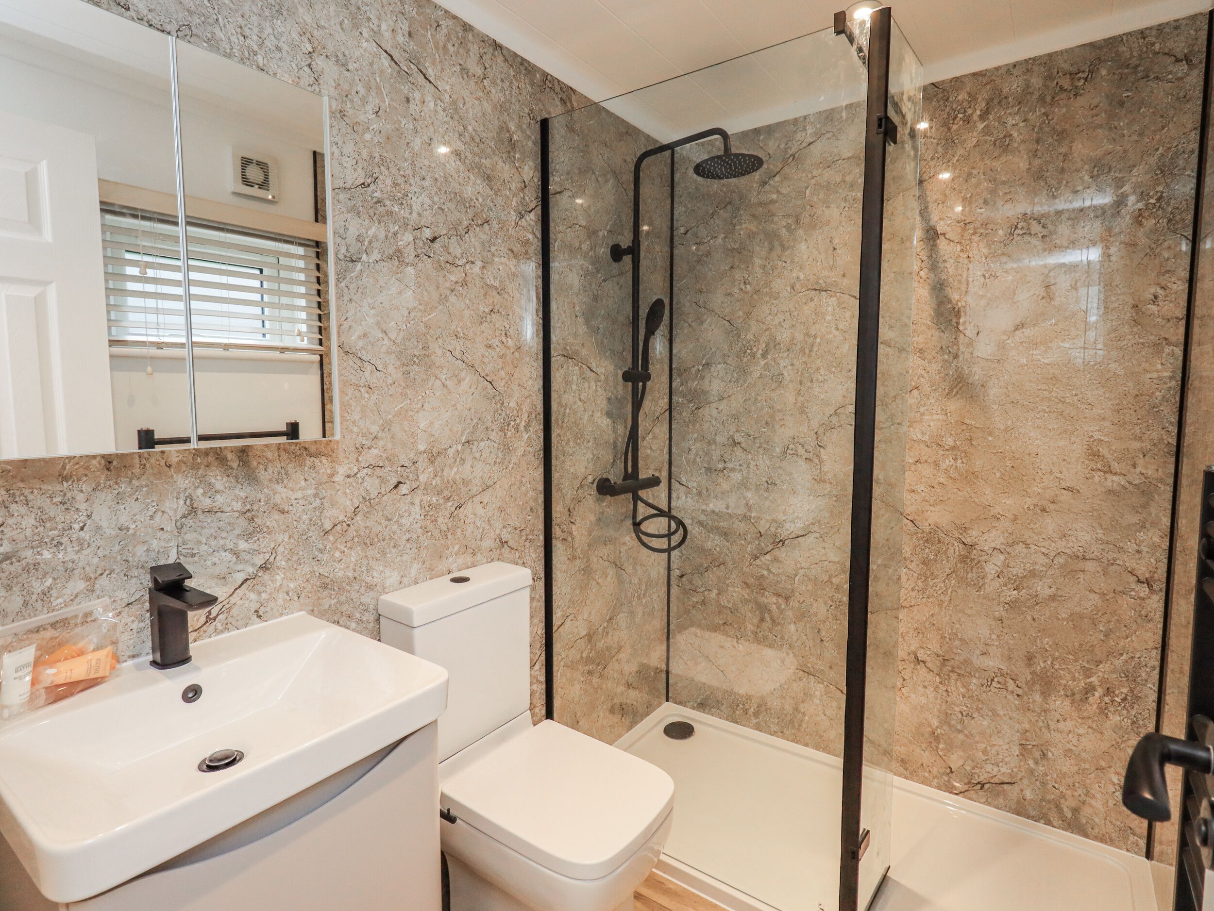 Un baño con lavamanos blanco, inodoro y ducha con mampara de vidrio.