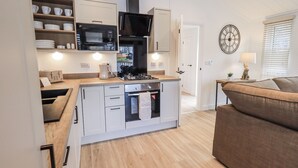 A compact kitchen with a microwave, oven, and sink, a dining area with a table and chairs, and a living room with a sofa and a lamp.