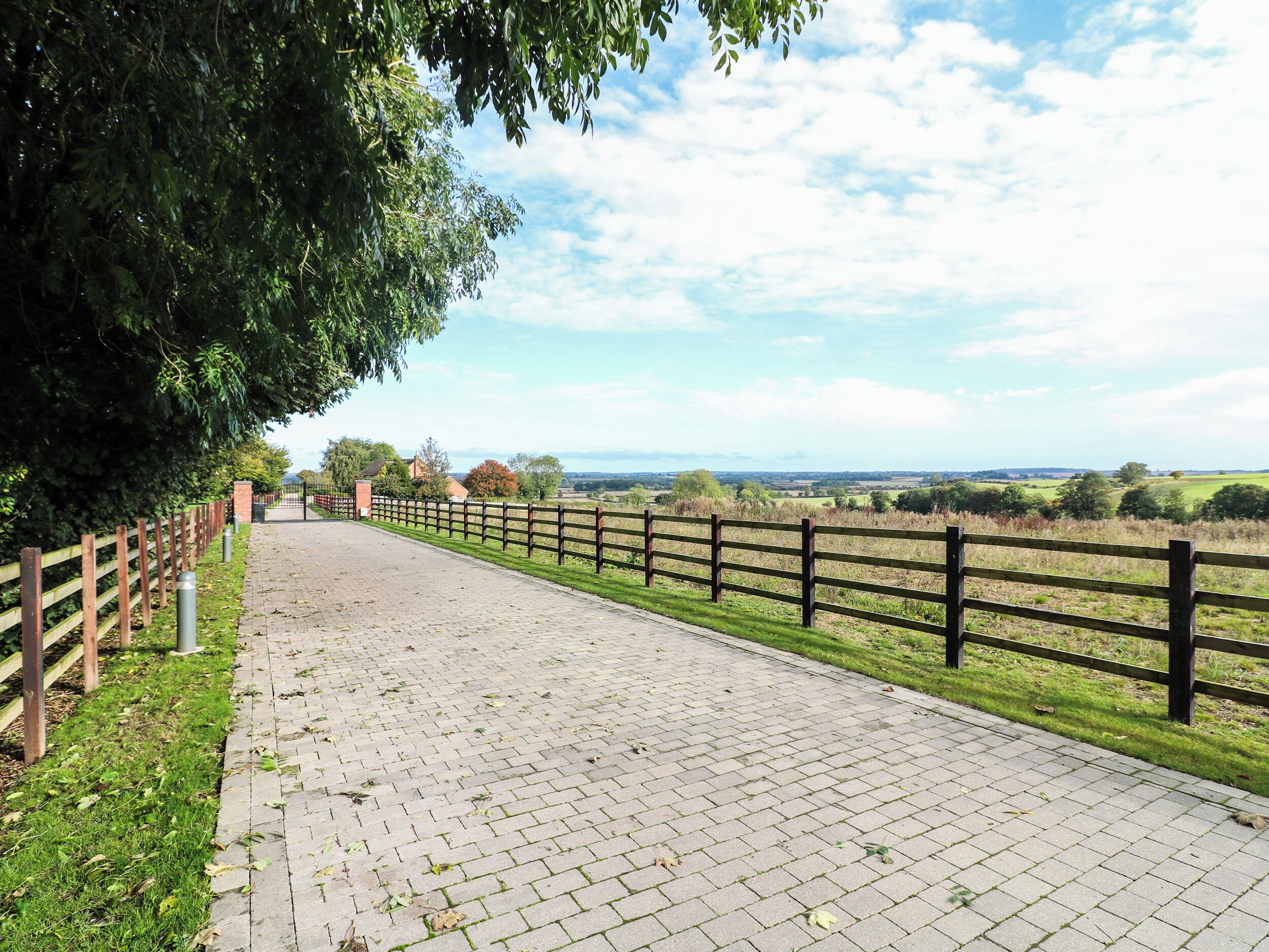 Un sendero pavimentado con una cerca de madera a un lado y un campo de césped al otro.