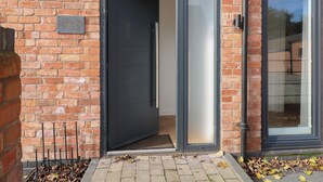 Een gebouw van baksteen met een zwarte deur en een glazen deur, een metalen bord met de tekst 'Buckingham House' en een metalen hek er voor.