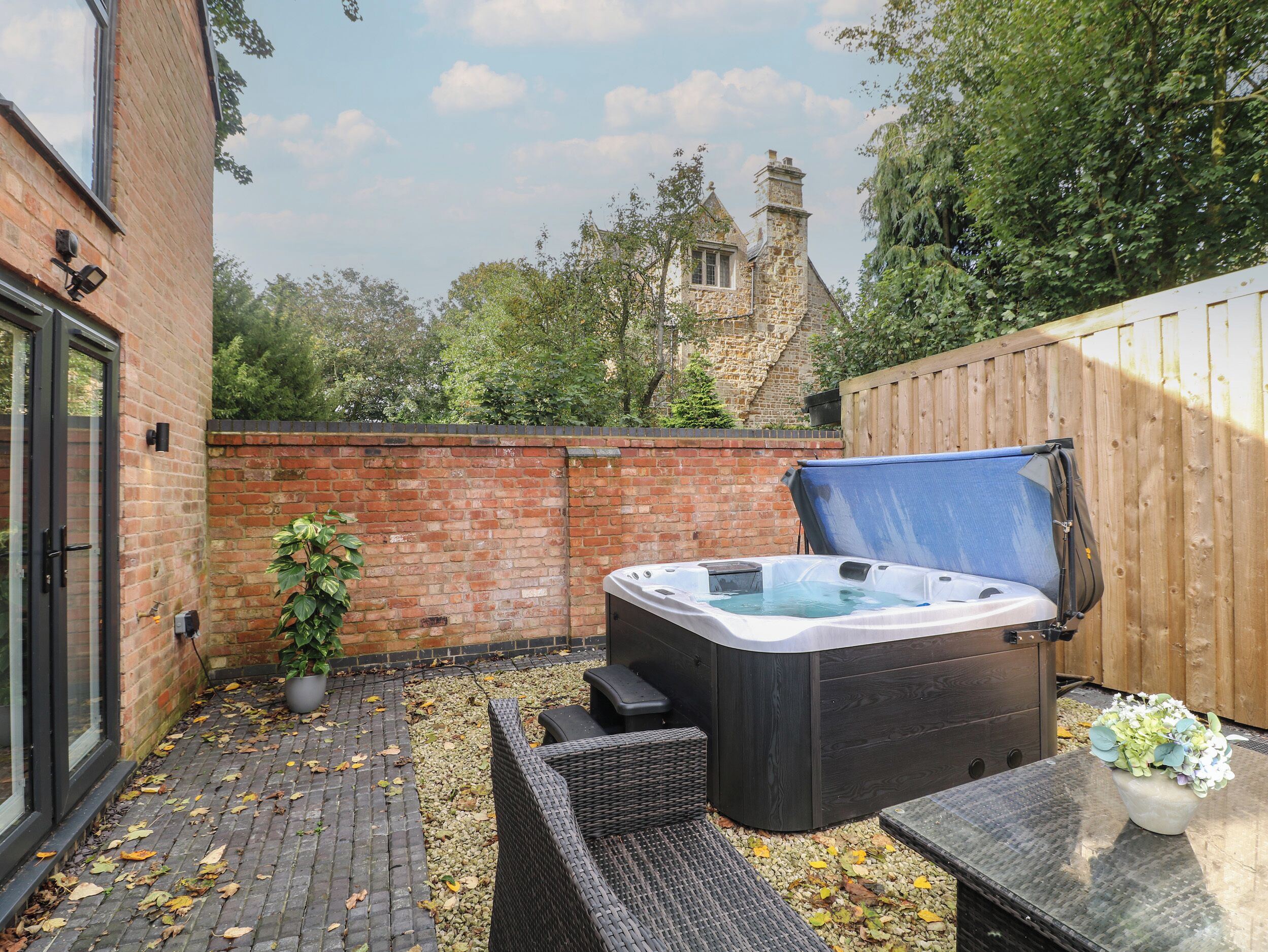 A hot tub in a backyard with a brick wall, wooden fence, and a stone building in the background.
