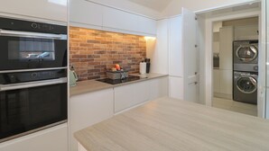 Een moderne keuken met een metselwerk achterwand, inbouwovens en een wasruimte met gestapelde wasmachines.
