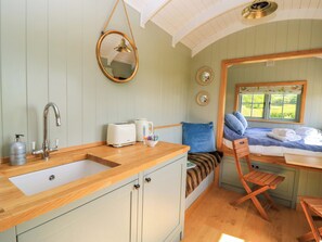 Una habitación acogedora con mostrador de madera, lavamanos, hervidor, tostadora y ventana con vistas a la vegetación.