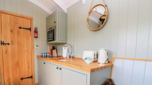 Une cuisine compacte avec un plan de travail en bois, un évier, un four à micro-ondes et une bouilloire. On y trouve une porte en bois et un miroir accroché au mur.