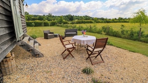 Un espace extérieur aménagé avec une table et des chaises, un sol en gravier et une vue sur un champ verdoyant.