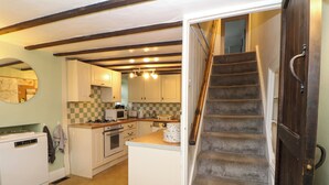 Une cuisine avec des meubles blancs, un four à micro-ondes, une cuisinière et un évier. Un escalier mène à un autre niveau.