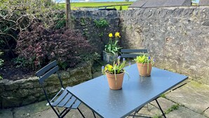 Un mur de pierre, une table en métal et deux chaises, le tout dans un jardin.