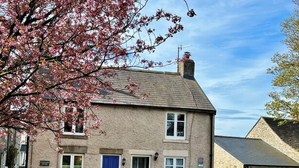 Une charmante maison de campagne en pierre, à deux étages, avec une porte bleue, des fenêtres blanches et une cheminée en pierre.