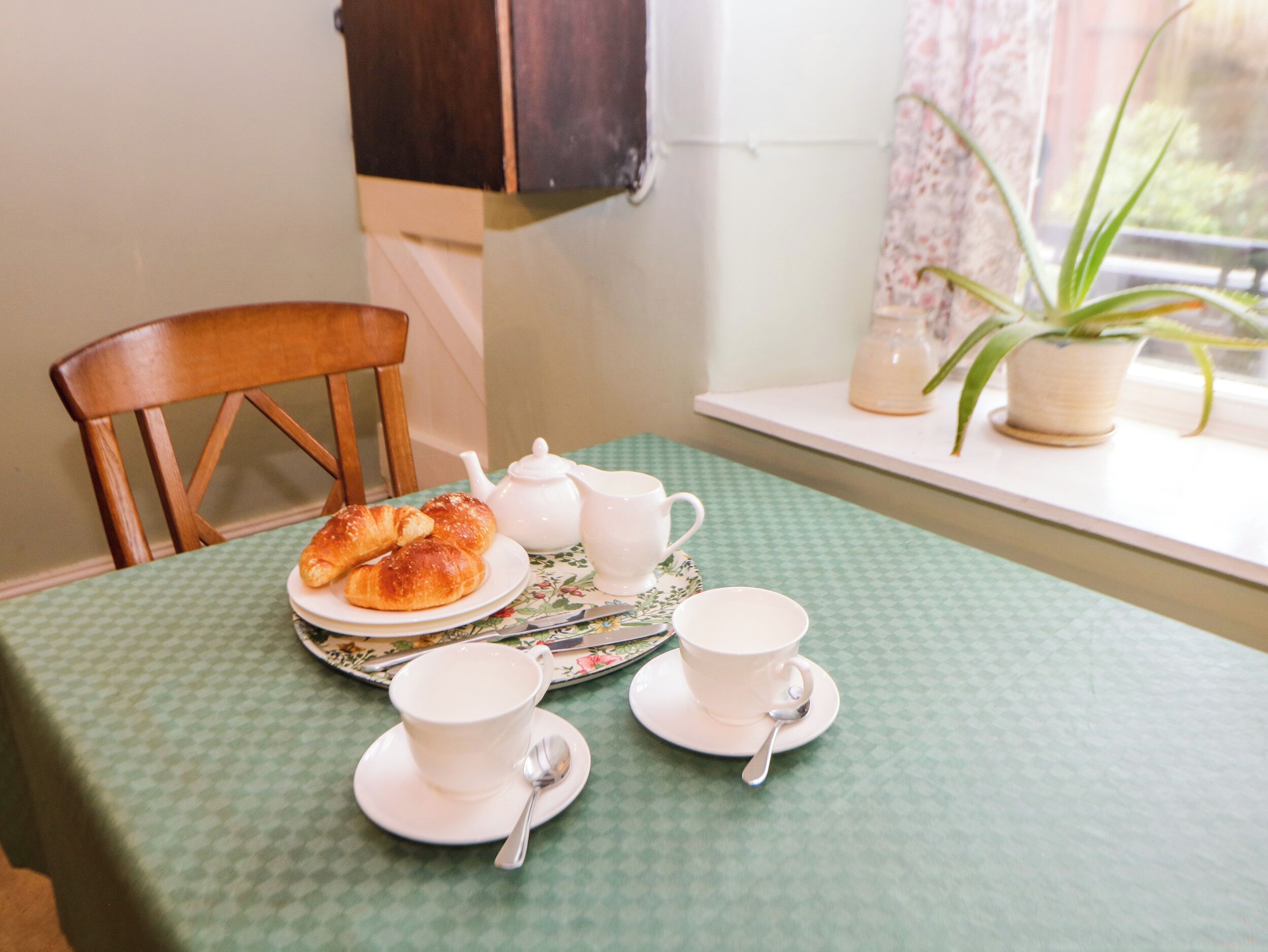 A table set with croissants, a teapot, cups, and a saucer.