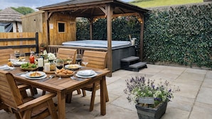 Un espace extérieur aménagé pour les repas, avec des tables et des chaises en bois, un jacuzzi et un gazebo en bois.