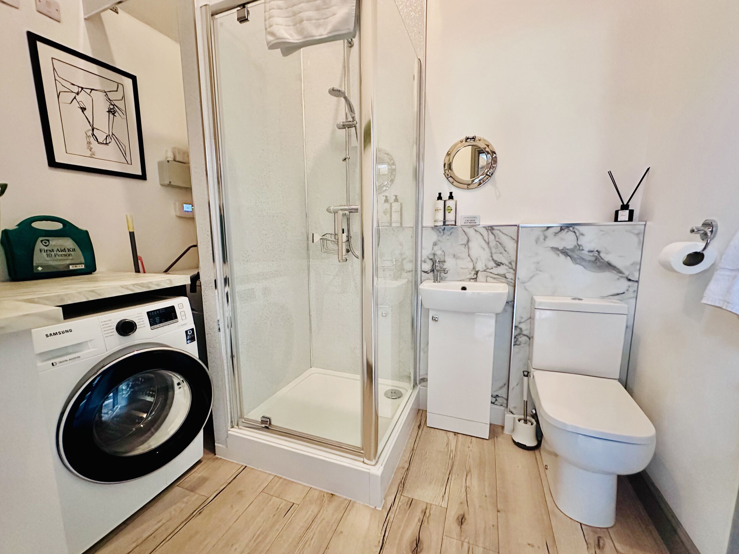 A modern bathroom with a glass-enclosed shower, a washing machine, a sink, and a toilet.