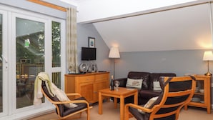 Una sala de estar acogedora con un sofá, dos sillones, una mesa de centro de madera y un televisor sobre un mueble.