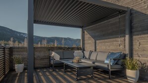 An outdoor seating area with a wooden deck, a covered section, and a view of mountains.
