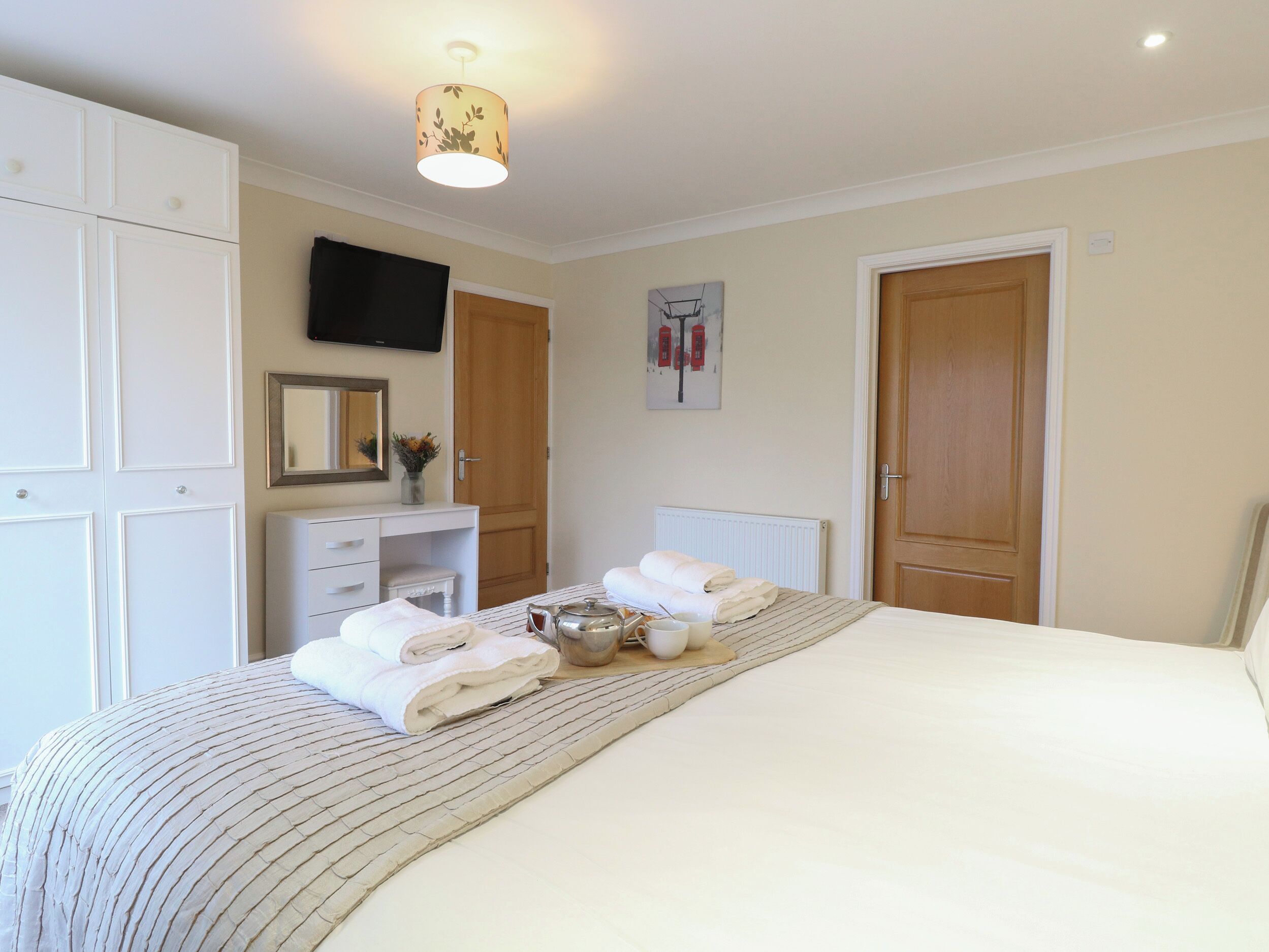 A bedroom with a bed, a dresser, a mirror, a television, and two doors.