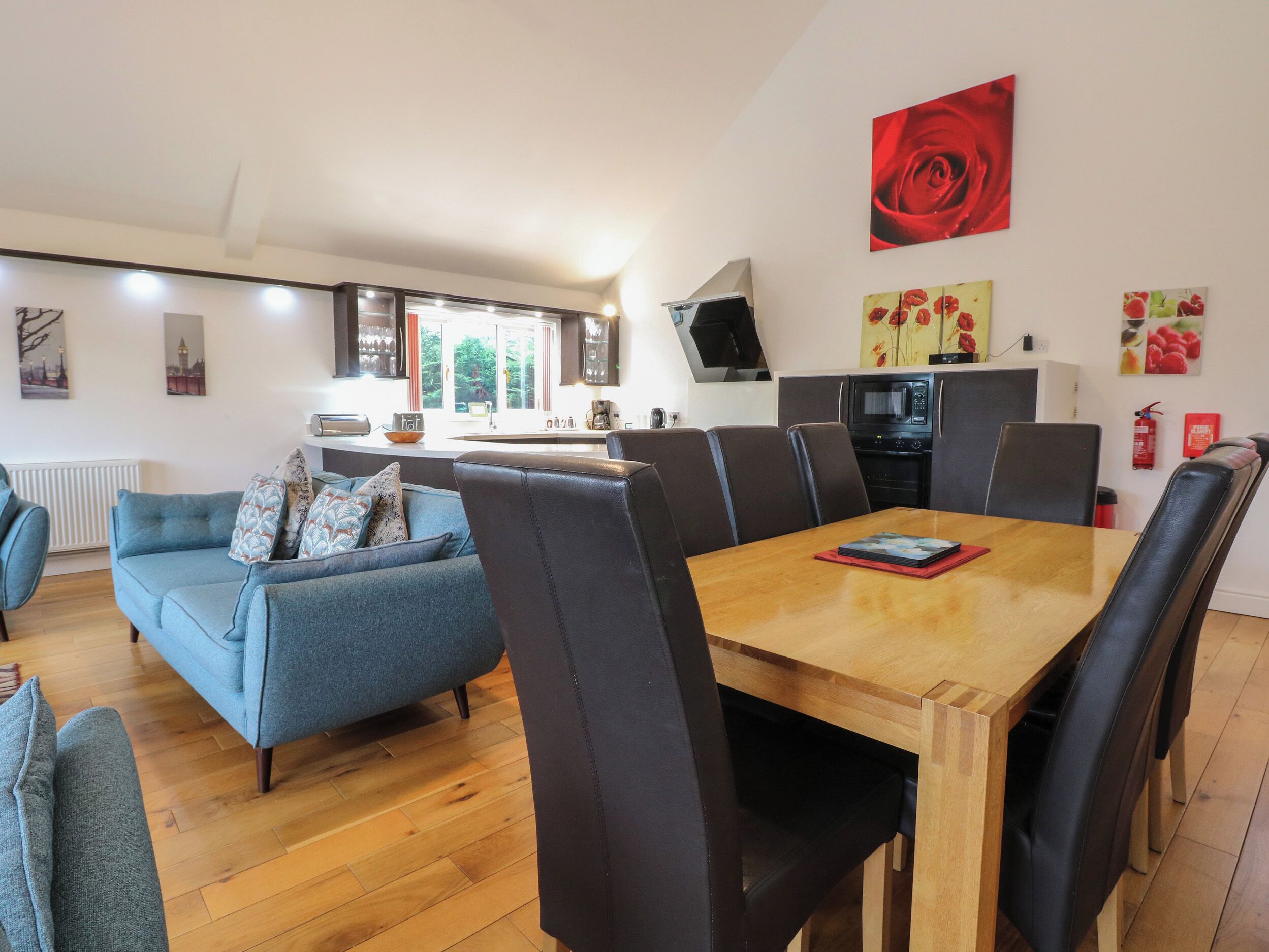 Una sala moderna con un sofá, una mesa de comedor con sillas, una zona de cocina con microondas y un ventanal grande.