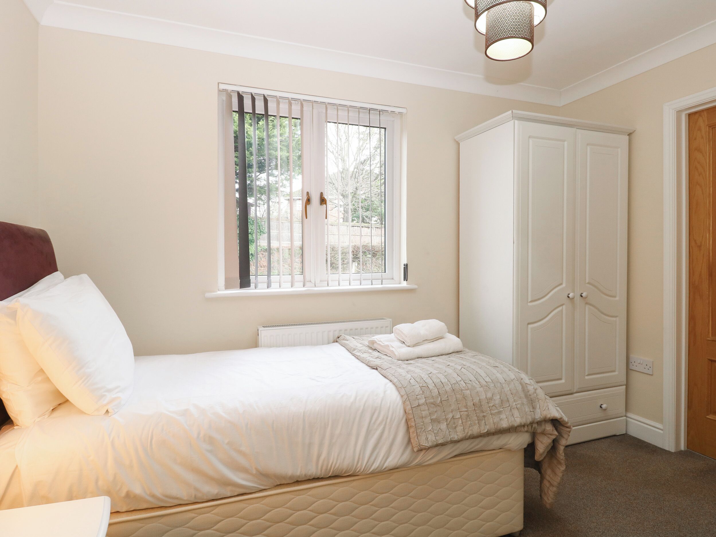 A bedroom with a bed, a window with blinds, a radiator, a wardrobe, and a door.