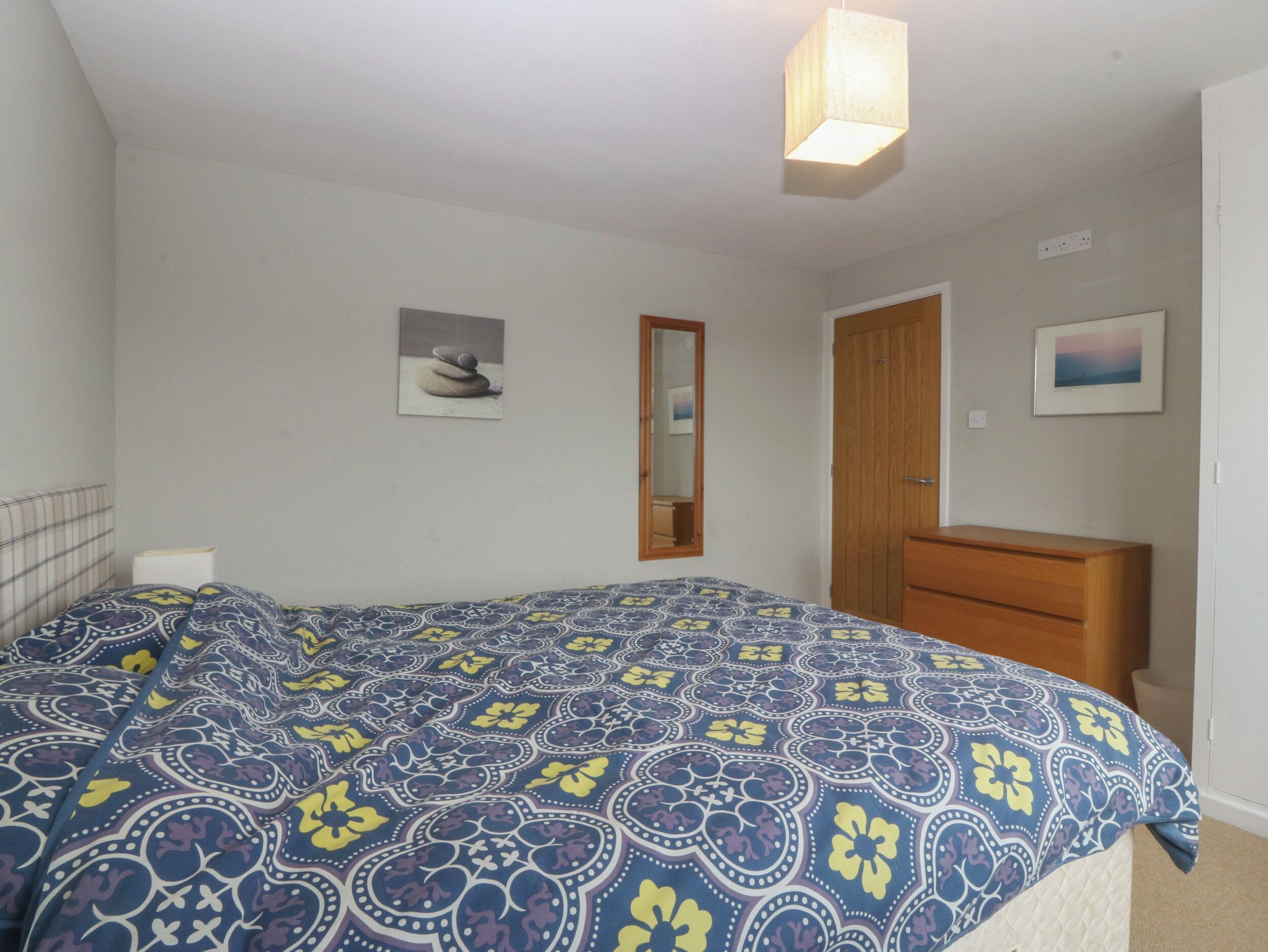 A bedroom with a bed, dresser, and two framed pictures on the wall.
