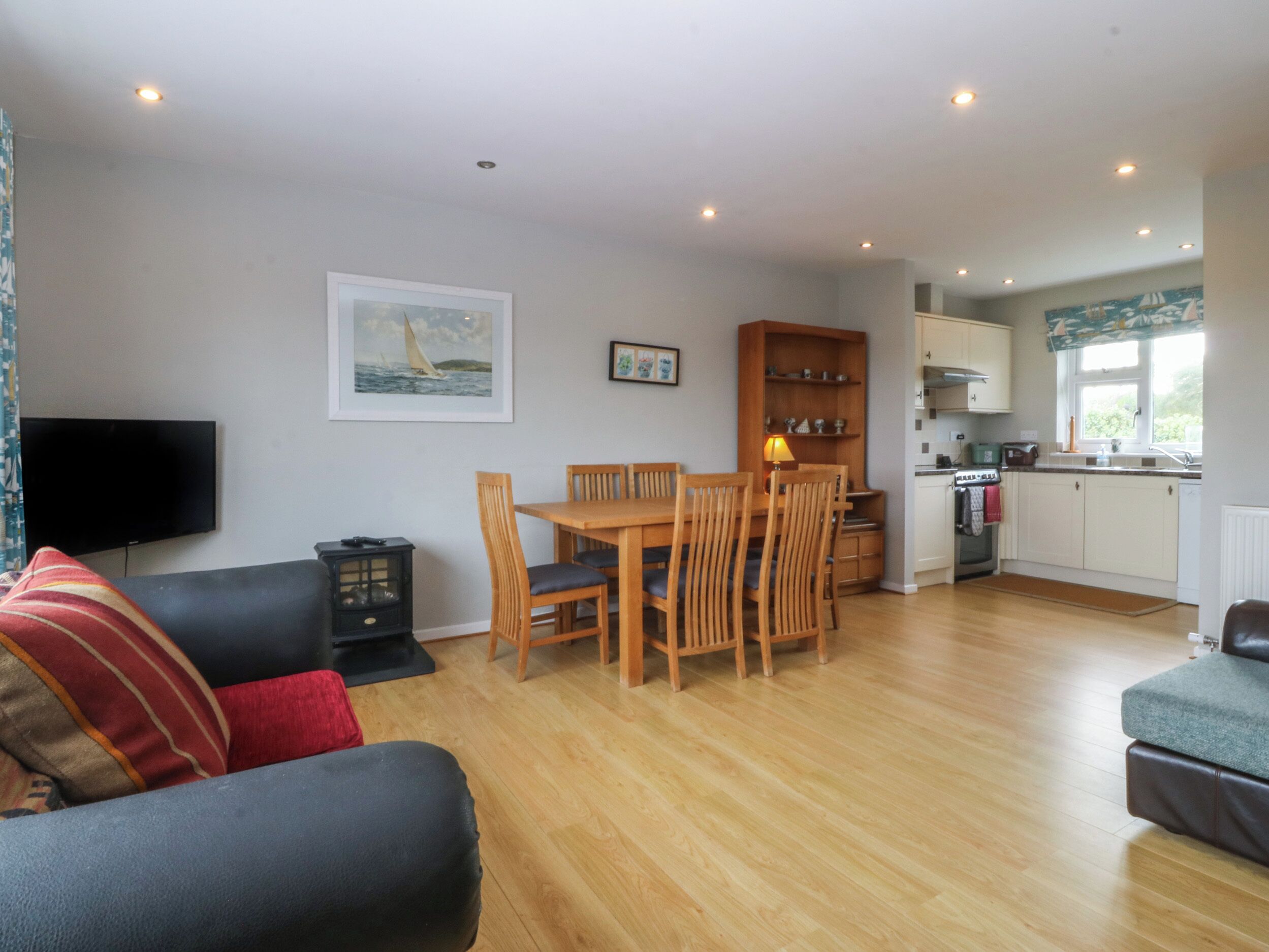 A living room with a sofa, a dining table with chairs, a TV, and a kitchen area with cabinets and a window.