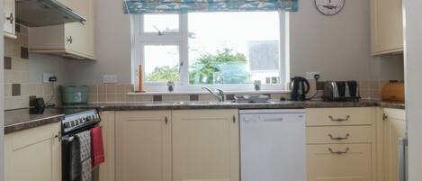 A kitchen with white cabinets, a built-in oven, a dishwasher, and a window with a sailboat curtain.