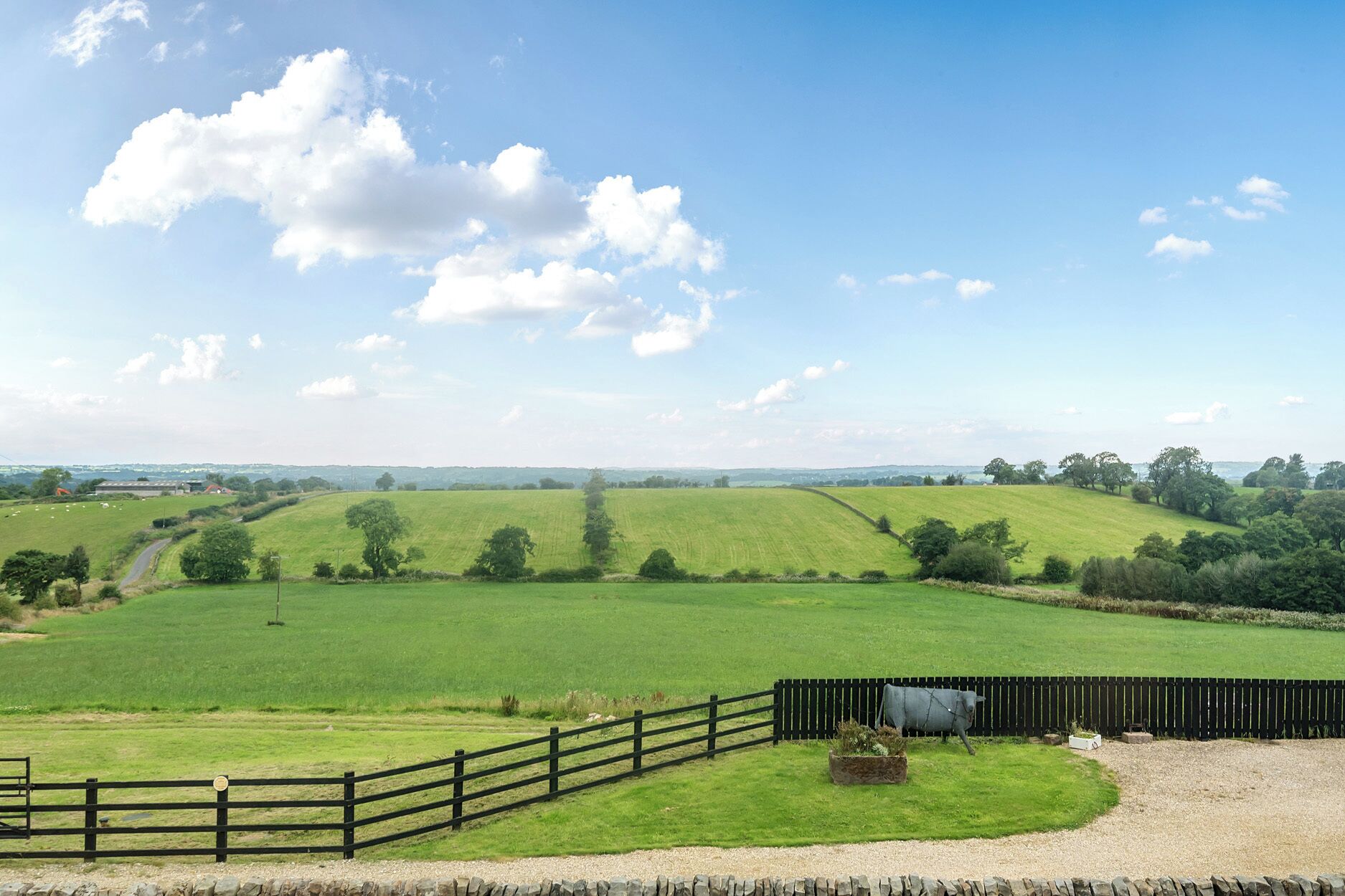A rural landscape with rolling green fields, a stone wall, and a wooden fence.