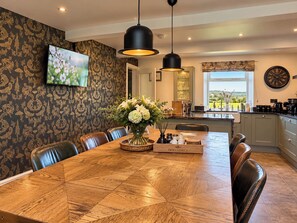 A dining area with a wooden table, chairs, a vase of flowers, and a television on the wall. - Hollydale (Leek)