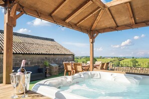 A hot tub under a wooden pergola with a stone building in the background and a view of the countryside. - Hollydale (Leek)