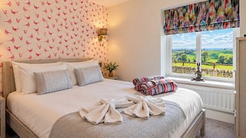 Un dormitorio con una cama grande, una pared con estampado de pájaros, una ventana con vistas y una lámpara roja.