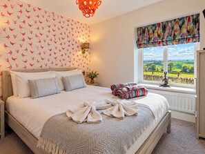 A bedroom with a large bed, a wall with a bird pattern, a window with a view, and a red light fixture. - Hollydale (Leek)