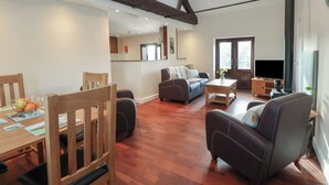 Uma sala de estar ampla com uma mesa de jantar de madeira, cadeiras, um sofá e uma televisão.