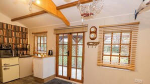 A kitchen with wooden floors, a refrigerator, a microwave, a coffee maker, and a bookshelf filled with books. - The Cabin at Little Timbers (Ringwood)