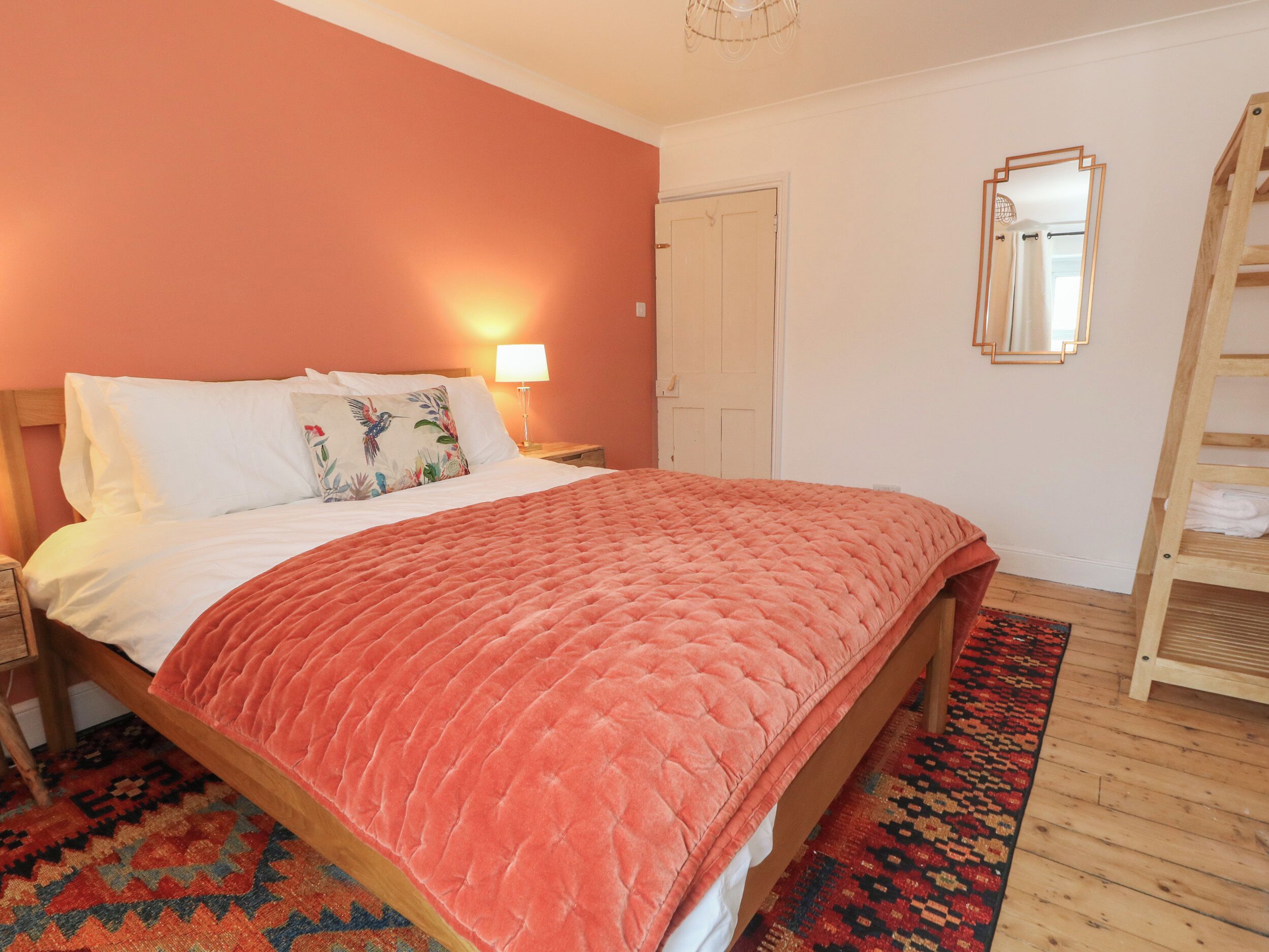 A bedroom with a bed, a nightstand, a lamp, a wooden ladder, a door, and a mirror.