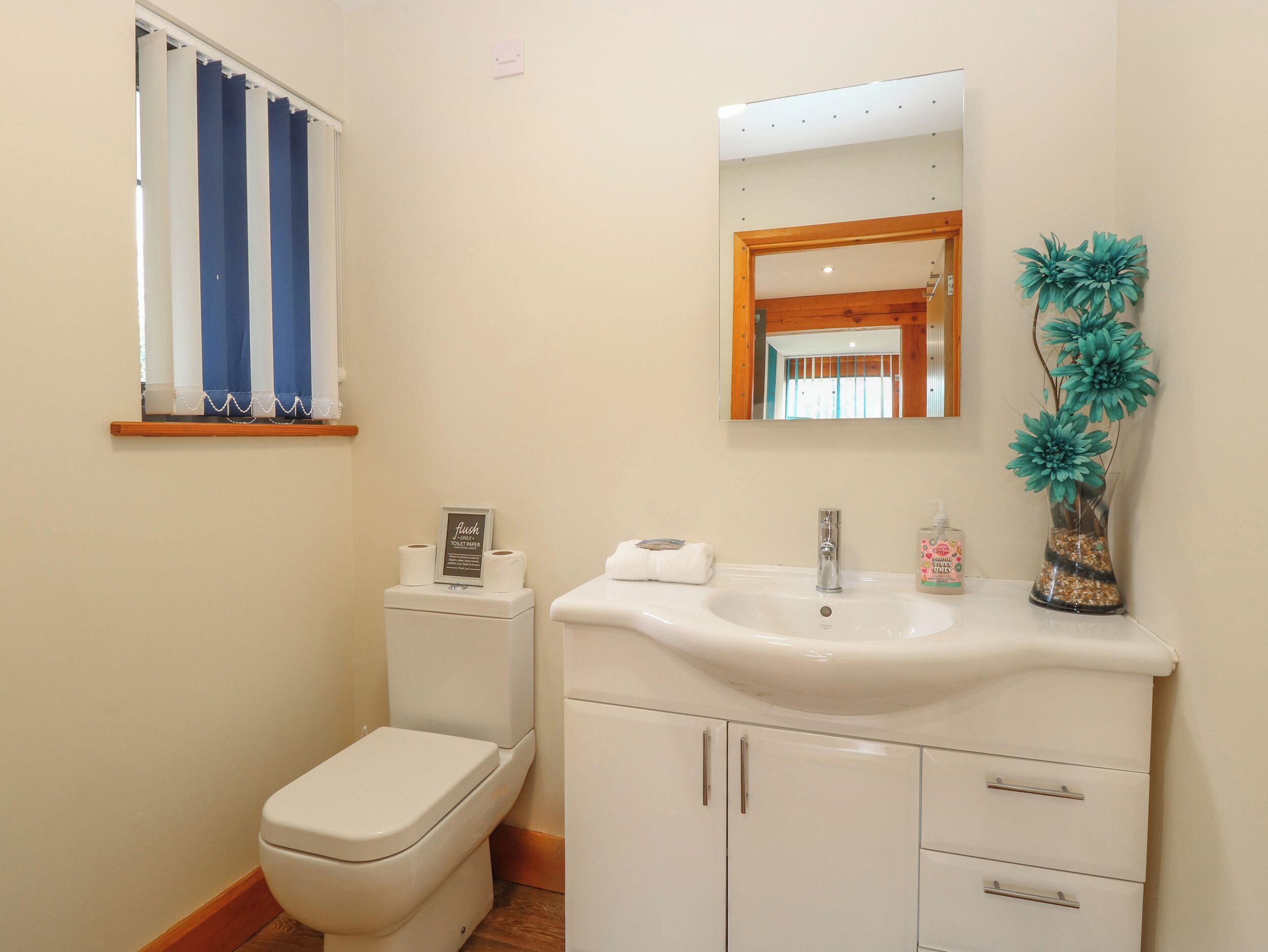 A bathroom with a toilet, sink, mirror, and a window with curtains.