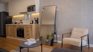 Una cocina moderna con armarios de madera, un microondas y una cafetera. Hay una mesa redonda con una caja y una planta. Un espejo grande está apoyado contra la pared.