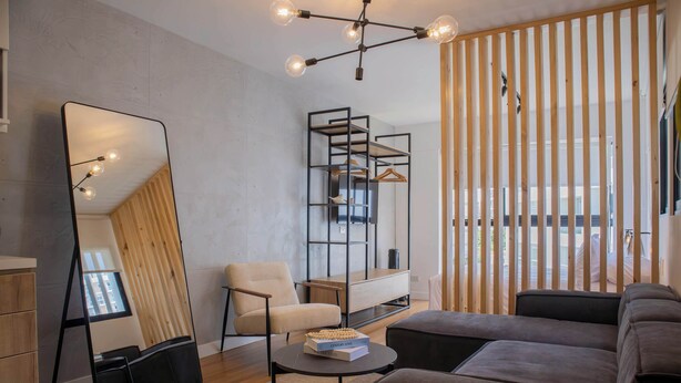 Una sala de estar moderna con un espejo grande, un sofá, un sillón, una mesita y una partición de madera con listones verticales.