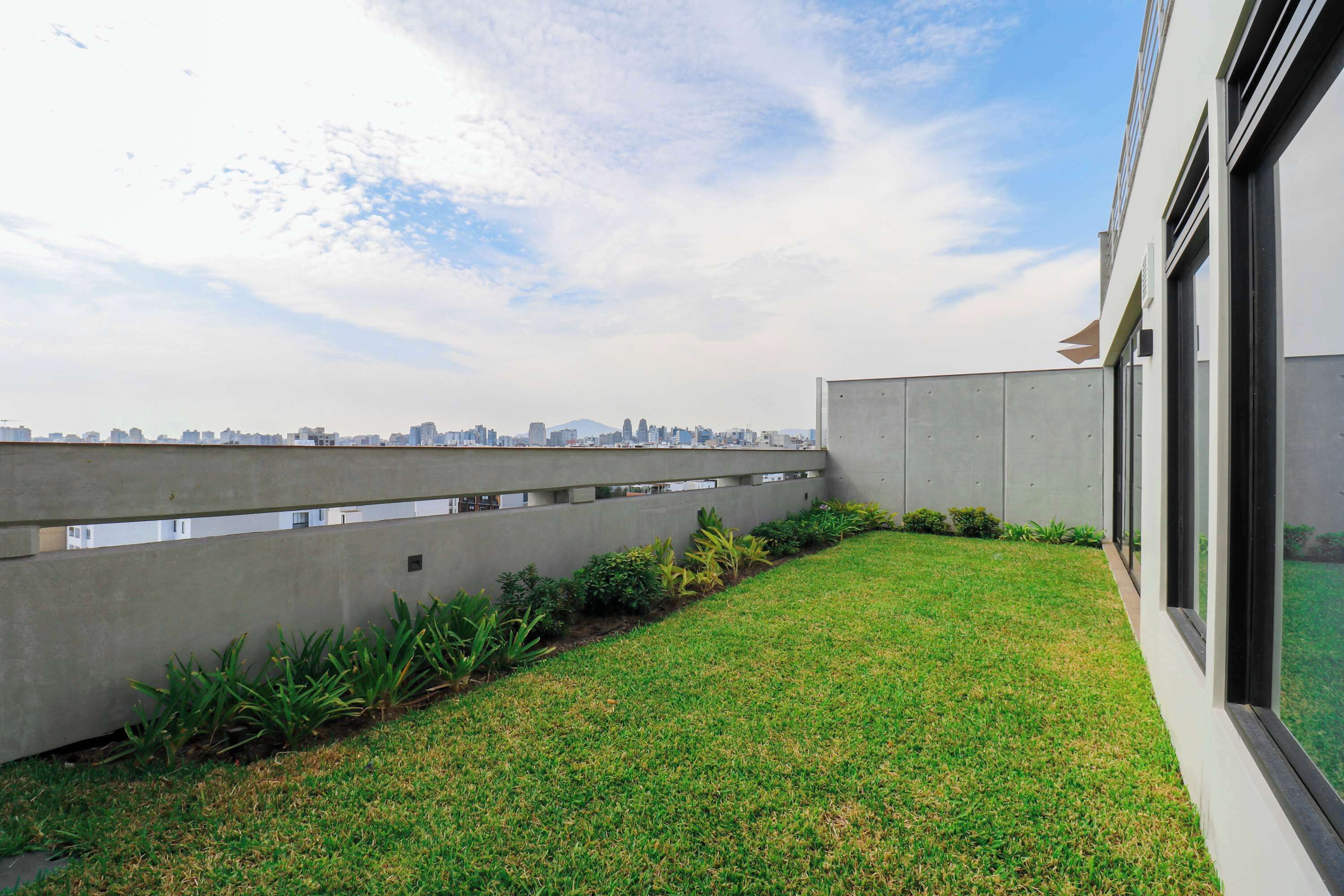 A modern building with a concrete facade, a grassy courtyard, and a city skyline in the background.
