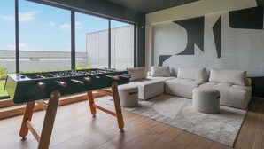 A modern living room with a foosball table, a sectional sofa, and a large window offering a view of the outdoors.