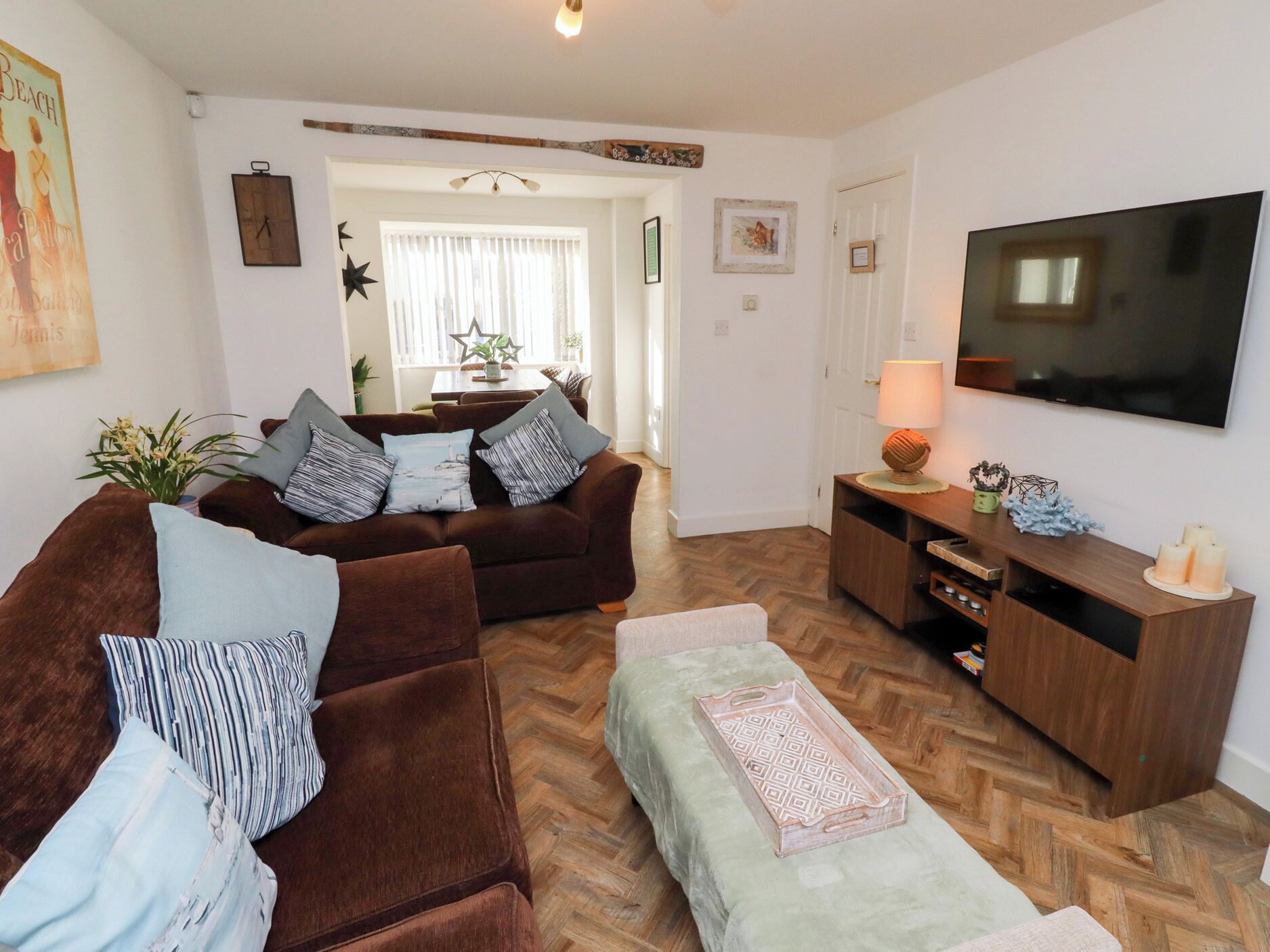 Un salón con un sofá marrón, una mesa de centro de madera, un televisor sobre un mueble de madera y un suelo con estampado de espiga.