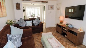 A living room with a brown sofa set, a wooden coffee table, a TV on a wooden stand, and a herringbone-patterned floor. - Coastal Retreat (Seahouses)