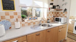 A kitchen with a sink, a microwave, and a window with a view of the outside. - Coastal Retreat (Seahouses)