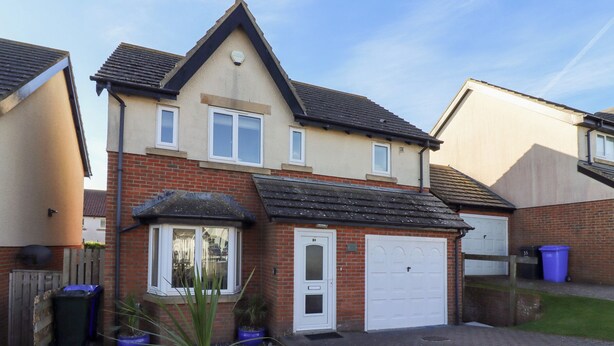 A two-story residential house with a garage, a small front garden, and a brick facade. - Coastal Retreat (Seahouses)