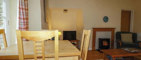 A cozy living room with a wooden dining table, chairs, a television, a fireplace, and a sofa.