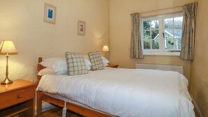 Ein Schlafzimmer mit einem Einzelbett, zwei Nachttischlampen, einem Fenster mit Vorhängen und zwei gerahmten Bildern an der Wand.