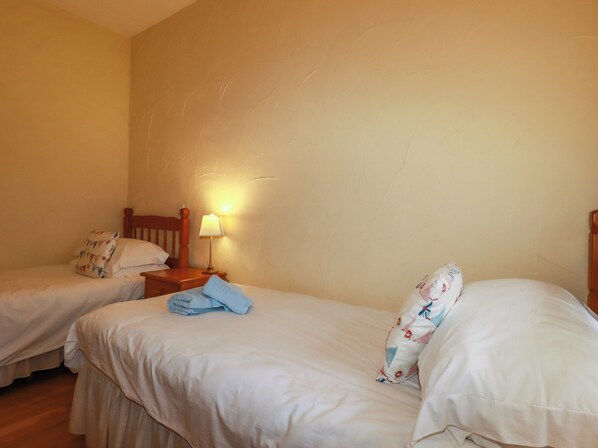 A hotel room with two single beds, a nightstand with a lamp, and a plain wall.