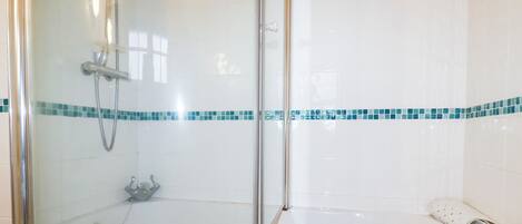 A bathroom with a glass-enclosed shower and a white bathtub with a blue-tiled border.
