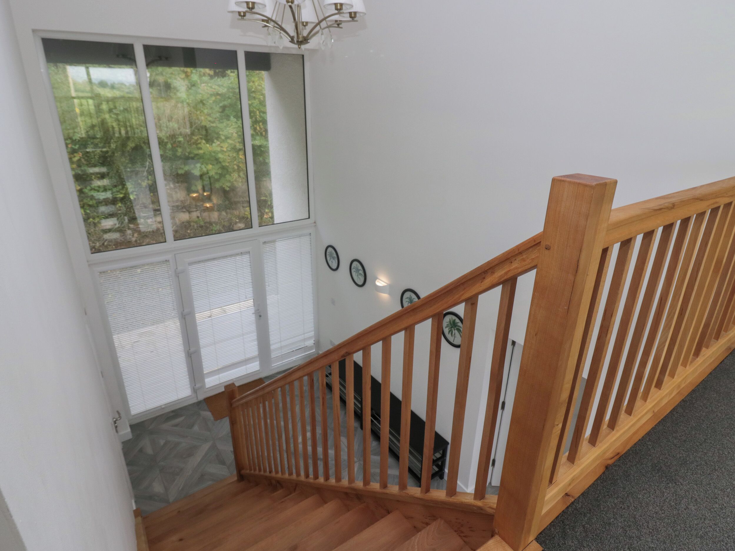 A wooden staircase with a railing, a window with blinds, and a wall-mounted light fixture.