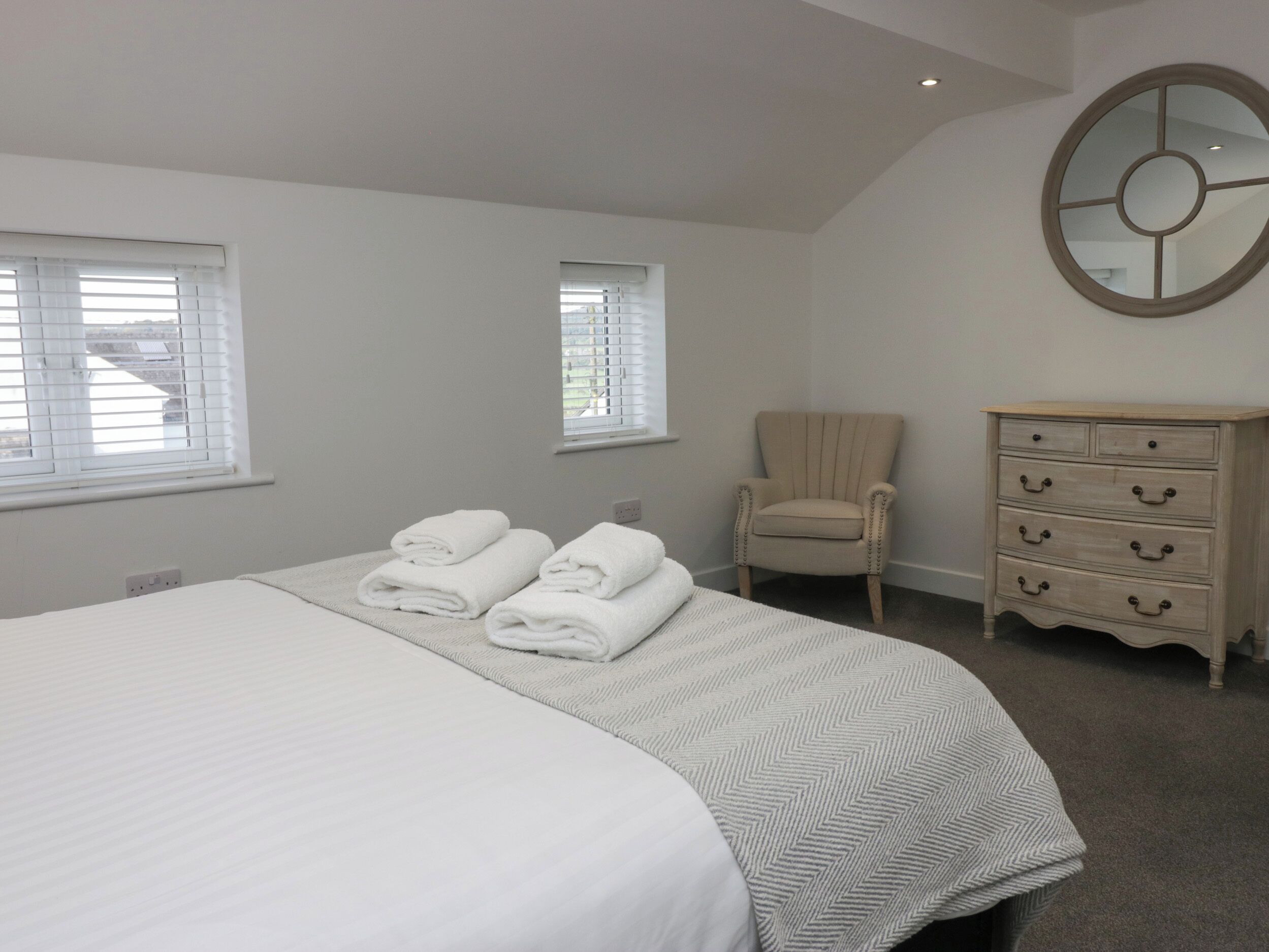 A hotel room with a bed, two windows, a chair, and a dresser.