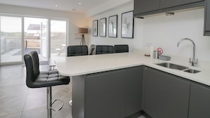A modern kitchen with a central island, bar stools, and a large window. - Edgemere Retreat (Grange-over-Sands)