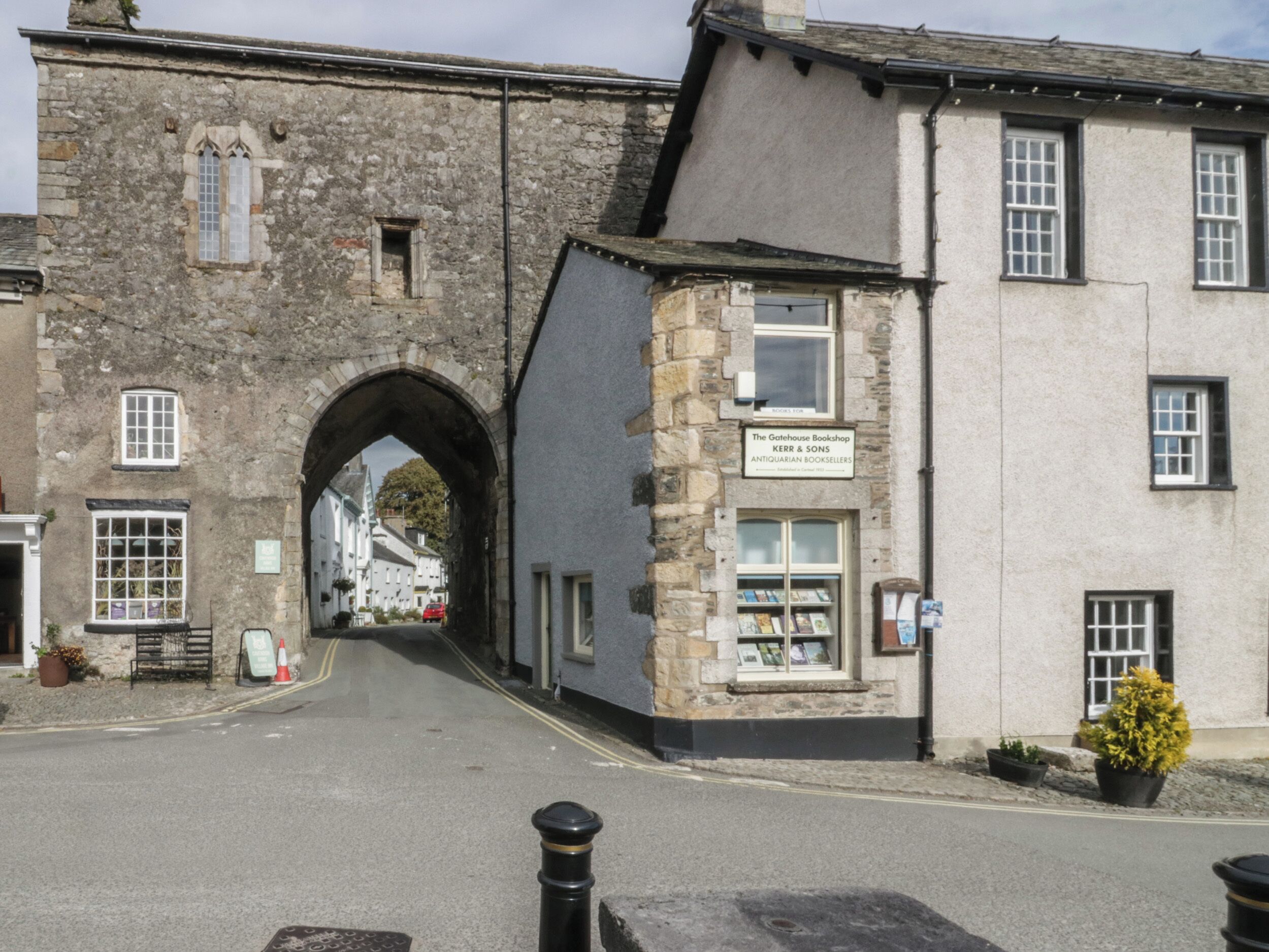 A street with a stone archway leading to a building with a sign for 'The Gatehouse Bookshop'.