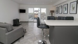 A modern kitchen with a dining area, a sofa, and a TV mounted on the wall. - Edgemere Retreat (Grange-over-Sands)