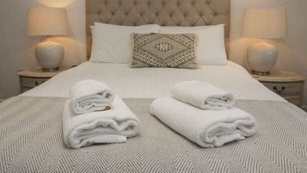 A neatly made bed with a tufted headboard, two bedside lamps, and a patterned throw pillow. - Edgemere Retreat (Grange-over-Sands)